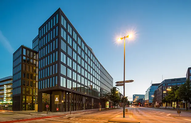 Moderne Bürogebäude mit Glasfassade und Straßenlaterne, gelegen an einer weitläufigen Straße.