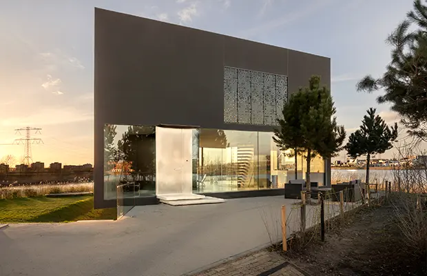 Modernes Gebäude mit Glasschiebetür, umgeben von Bäumen und einem Gehweg.