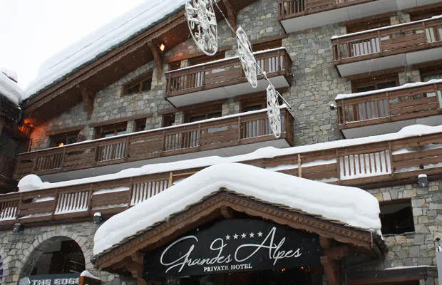 Hotel mit Holzfassade, schneebedecktem Dach und fünf-Sterne-Schild "Granges Alpes Private Hotel" am Eingang.