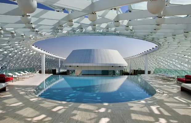 Ein moderner Innenpool mit einer künstlerischen, lichtdurchlässigen Überdachung. Rote Liegen entlang des Beckens.