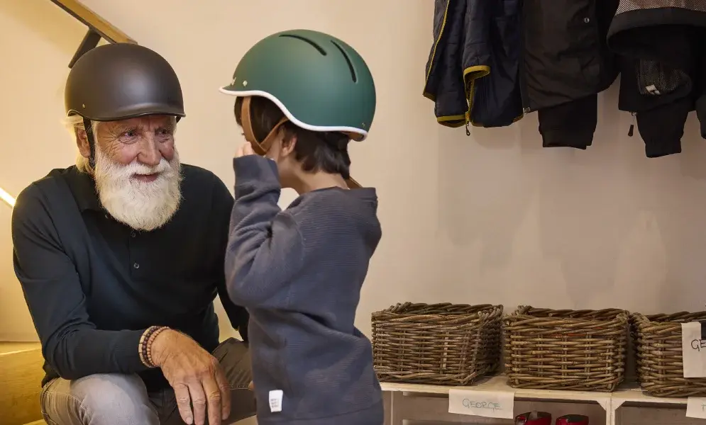 Ein älterer Mann und ein Kind tragen Helme, stehen nahe einer Treppe und unterhalten sich.