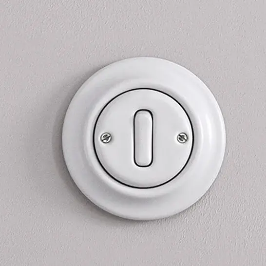 Weißer Lichtschalter in runder, flacher Abdeckung an einer Wand.