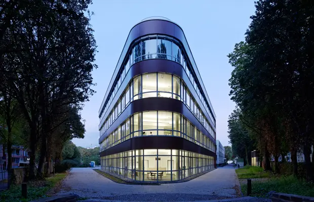 Moderne, dreigeschossige Bürogebäude mit großen Fensterfronten, umgeben von Bäumen und einem unbefestigten Weg.