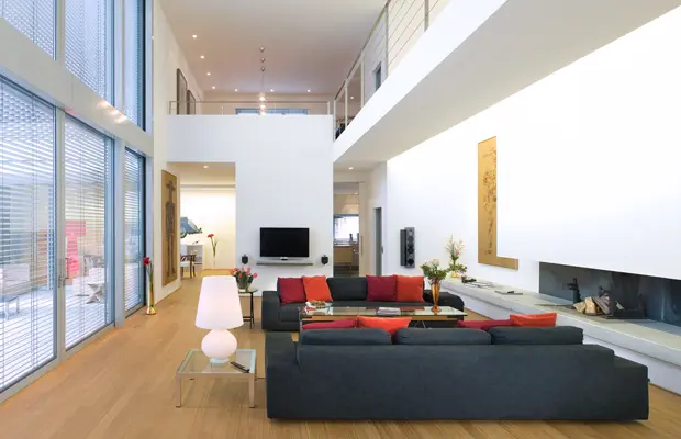 Modernes Wohnzimmer mit einem großen Sofa, Couchtisch und TV-Wand. Beleuchtet durch Fenster und eine Tischlampe.