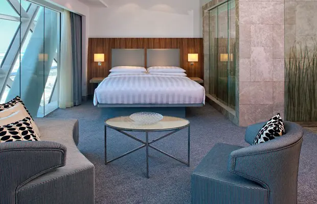 Modern Hotelzimmer mit einem Doppelbett, zwei Sesseln und einem Tisch in der Mitte. Helle und freundliche Einrichtung.