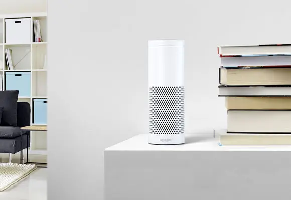 Ein weißer Lautsprecher mit einer perforierten Oberfläche steht neben einem Stapel Bücher auf einem Tisch.