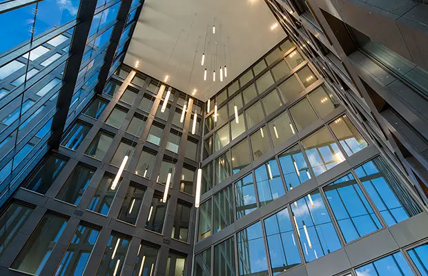 Innenansicht eines modernen Gebäudes mit großen Glasflächen und hängenden Lichtern, die den Raum beleuchten.