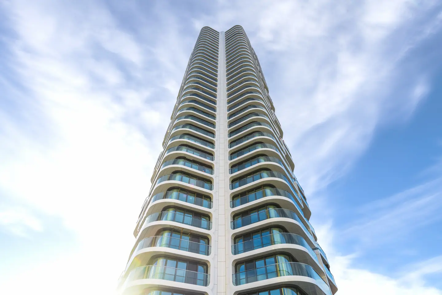 Hochhaus mit geschwungener Fassade und großen Fenstern, aufgenommen von unten gegen den Himmel.