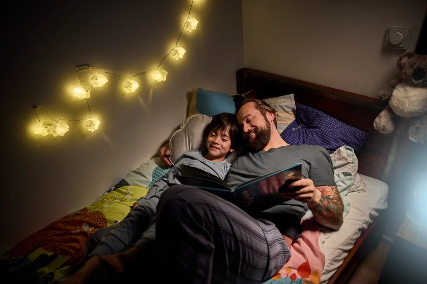 Vater und Kind lesen zusammen in einem Bett, umgeben von sanften Lichtern und einer gemütlichen Atmosphäre.